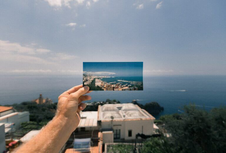 A person holding up a photo of a city and ocean to document procedures.